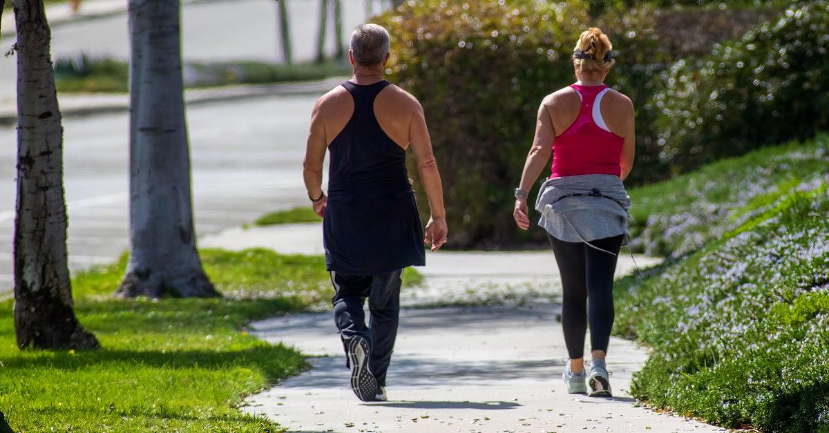 A couple walking along a sunny park pathway, enjoying outdoor exercise.