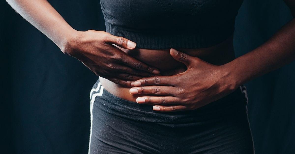 Close-up of a person pressing hands on abdomen, indicating discomfort or pain, against a black background.