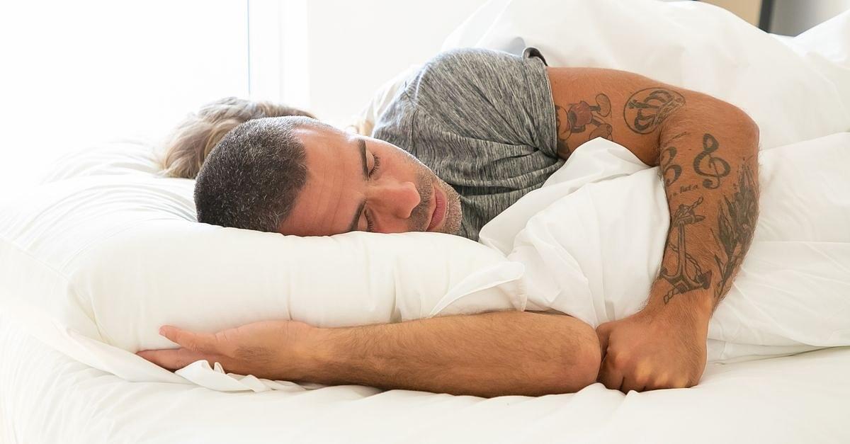 A man with arm tattoos sleeping peacefully in bed, illustrating rest and relaxation.