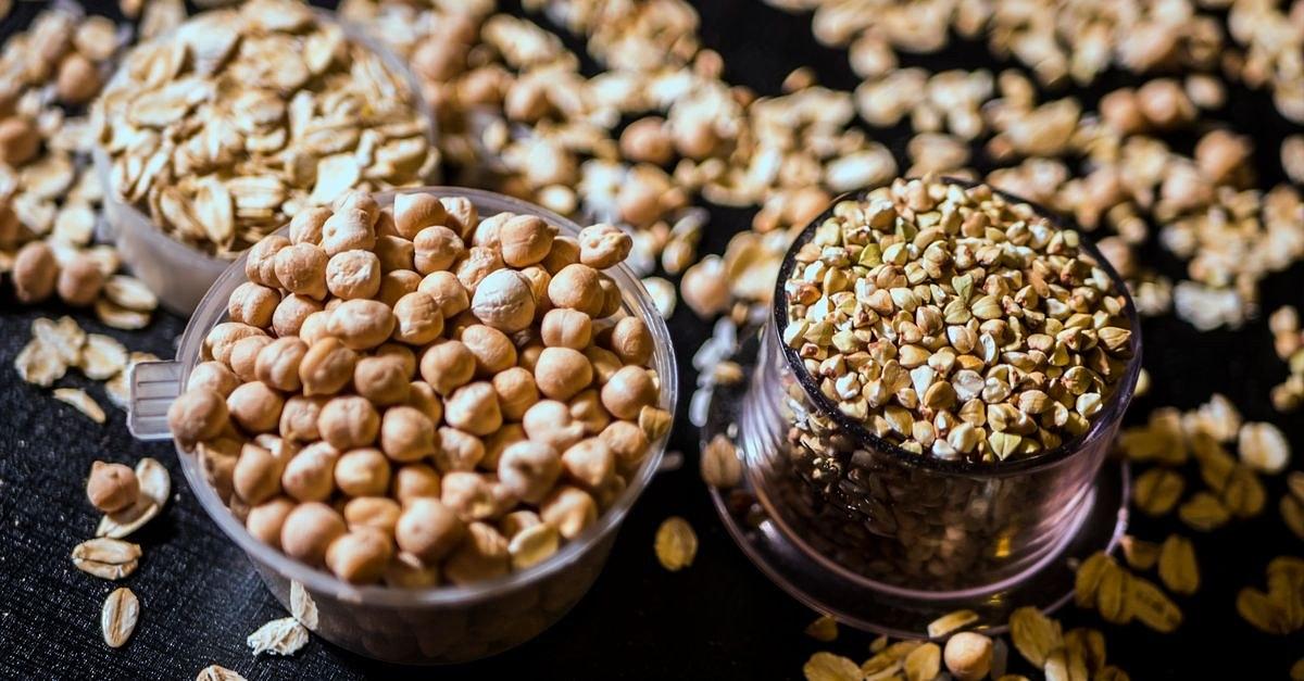 Close-up of assorted raw grains and seeds in cups on a dark background, showcasing variety and texture.