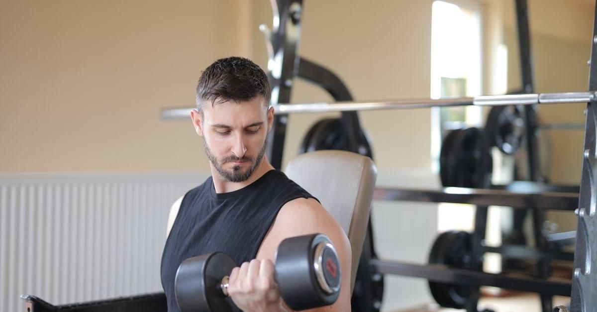 Adult male exercising with dumbbell in a gym, showcasing bicep strength training.