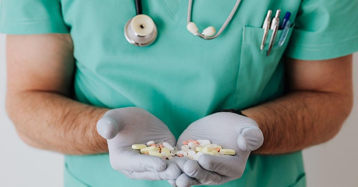 Crop unrecognizable medical worker in rubber disposable gloves holding in hands assorted pills