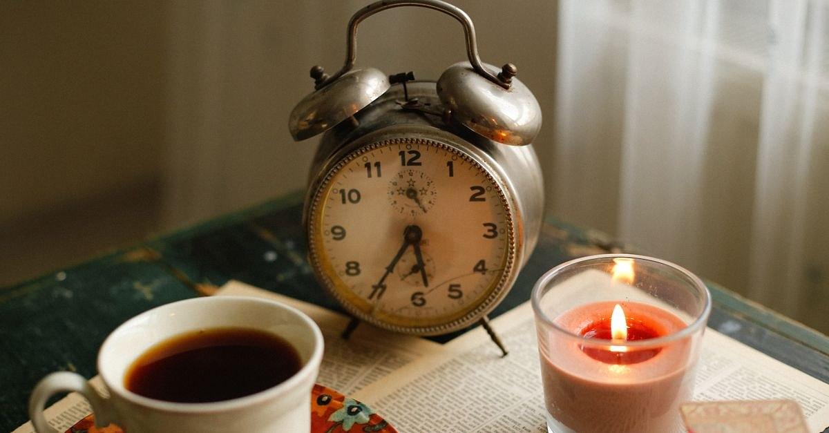 A cozy setting with a vintage alarm clock, coffee, and candle on a table.