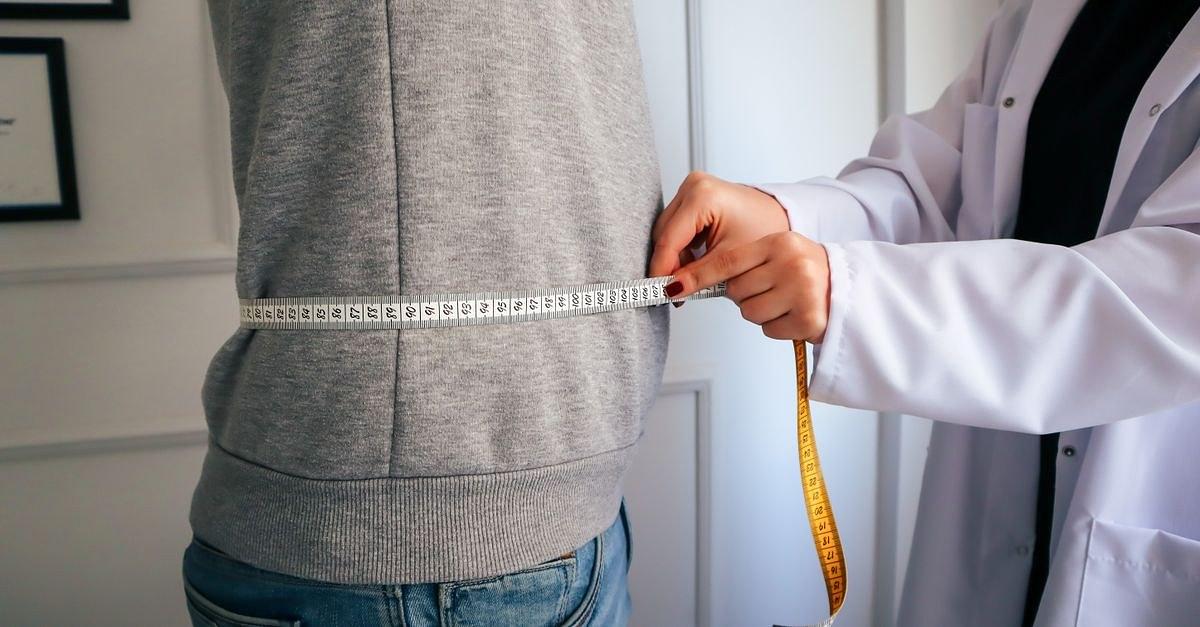 A nutritionist measuring a patient's waist using a tape in a clinical setting.
