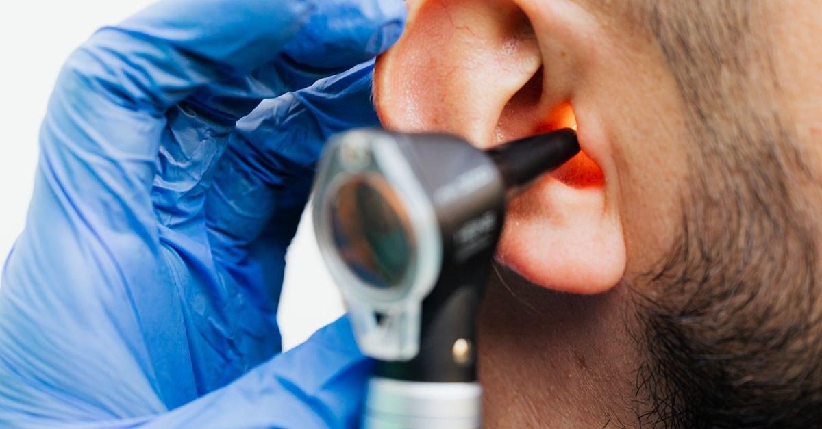Close-up of a doctor using an otoscope to examine a patient's ear in a clinical setting.
