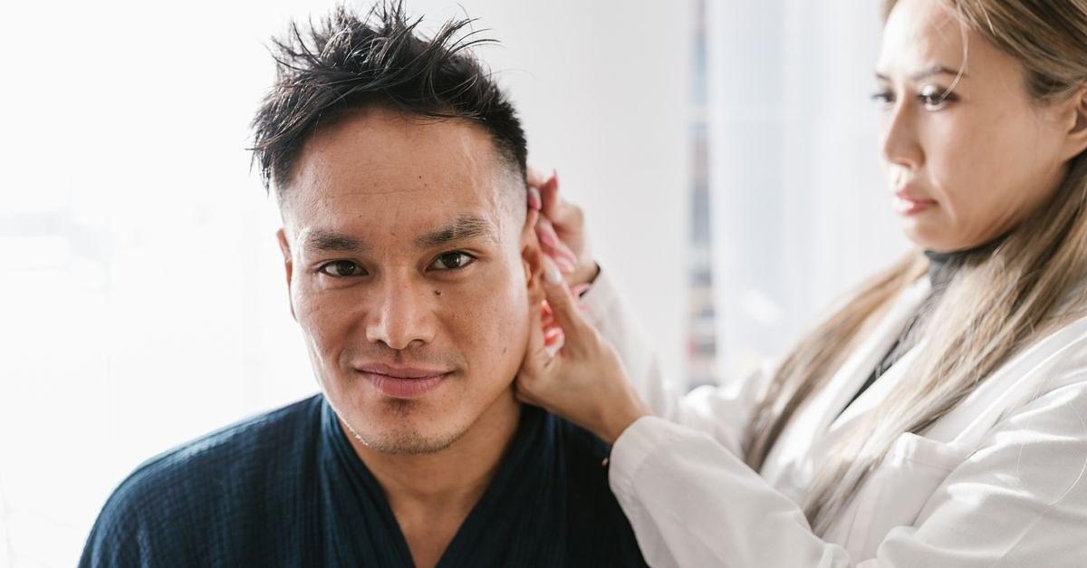 A doctor performs an ear examination on a patient in a well-lit clinic setting.