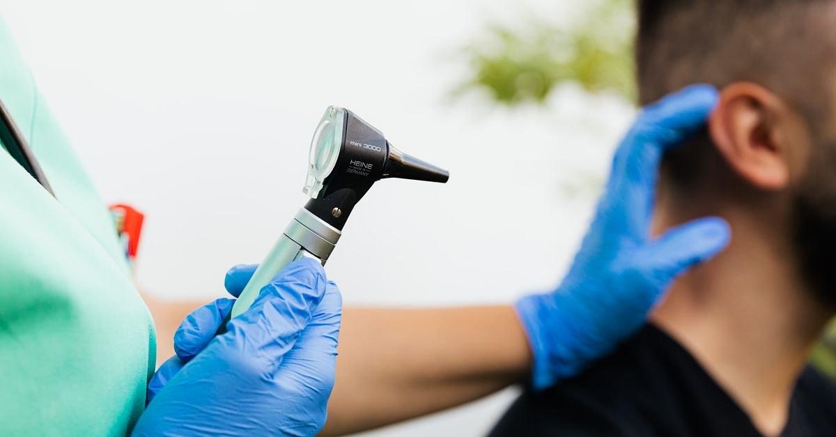 Healthcare professional examining patient's ear with an otoscope in a clinical setting.