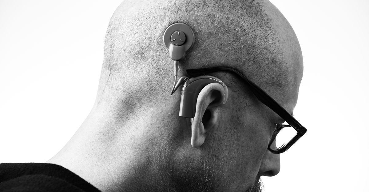 Black and white profile of a man wearing glasses and a hearing aid, studio shot.