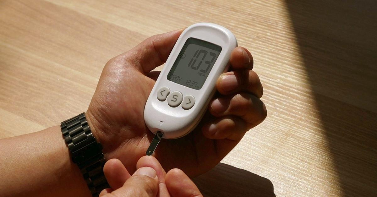 Close-up of a person checking blood glucose level with a meter in a sunny room, hands visible.
