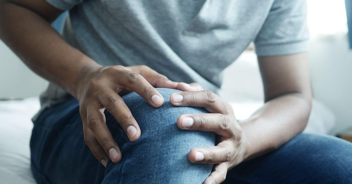 Close-up of a man holding his knee, capturing a moment of discomfort in a casual indoor setting.