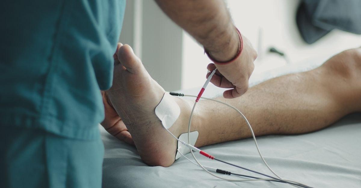 Close-up of a healthcare worker examining a patient's foot with medical equipment in a hospital setting.