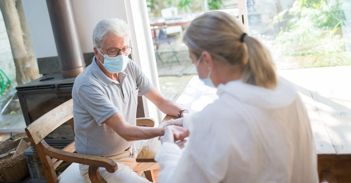 A healthcare worker examining a senior man at home with face masks during the pandemic.