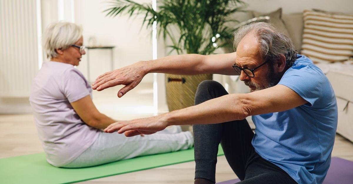 Elderly couple practicing yoga indoors with focus on wellness and fitness.
