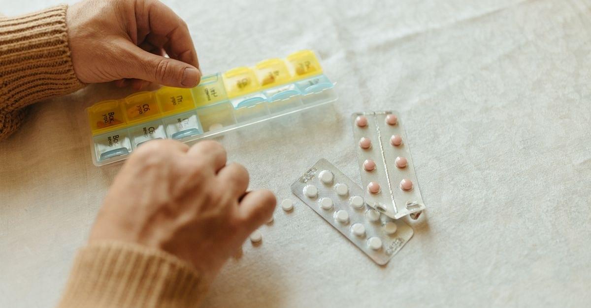 Close-up of hands organizing tablets into a weekly pillbox for daily medication management.